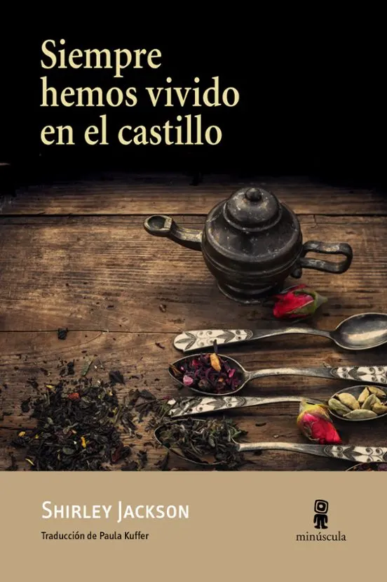 Sobre un fondo negro aparece el título en grandes letras color crema, ocupando la parte superior izquierda. En la mitad inferior se ve una mesa de madera envejecida con una tetera antigua de metal, varias cucharas decoradas llenas de hojas de té y especias, pétalos y pequeños capullos de rosa esparcidos, creando una atmósfera oscura y misteriosa. En la franja inferior, de color beige, figuran el nombre de la autora, Shirley Jackson, el crédito de la traductora, Paula Kuffer, y el logotipo de la editorial Minúscula.
