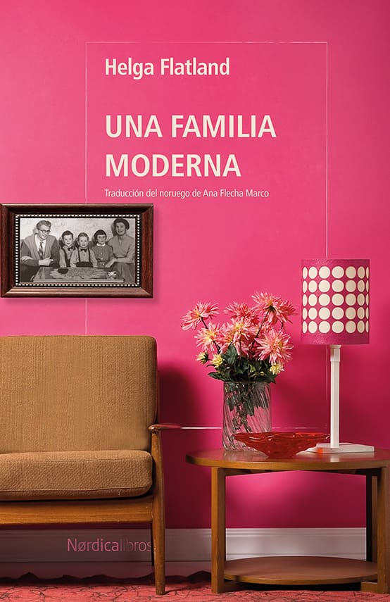 Sobre un fondo rosa intenso aparecen el título y el nombre de la autora en letras blancas. La escena muestra un salón de estilo retro con un sofá marrón, una mesa auxiliar de madera con un jarrón de flores y una lámpara de sobremesa estampada. En la pared cuelga una fotografía antigua de una familia sentada alrededor de una mesa.